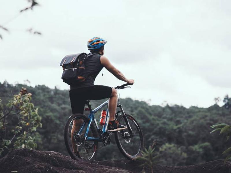 Ciclista su mountain bike osserva il panorama verdeggiante con zaino e casco.